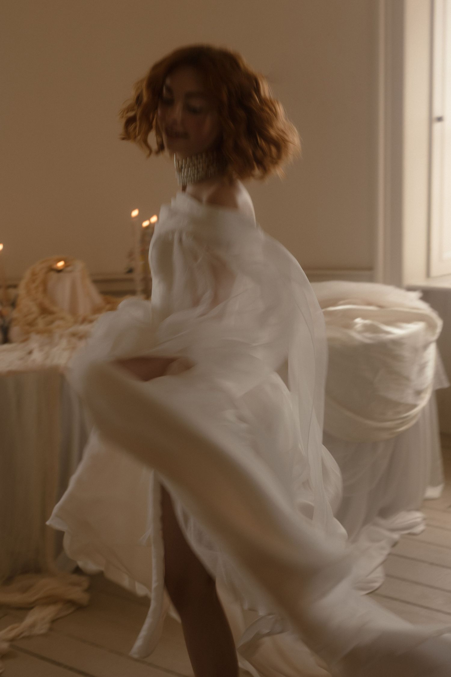 An artistic photograph of a blurred figure in flowing white fabric spinning and twirling in an ethereal interior setting.