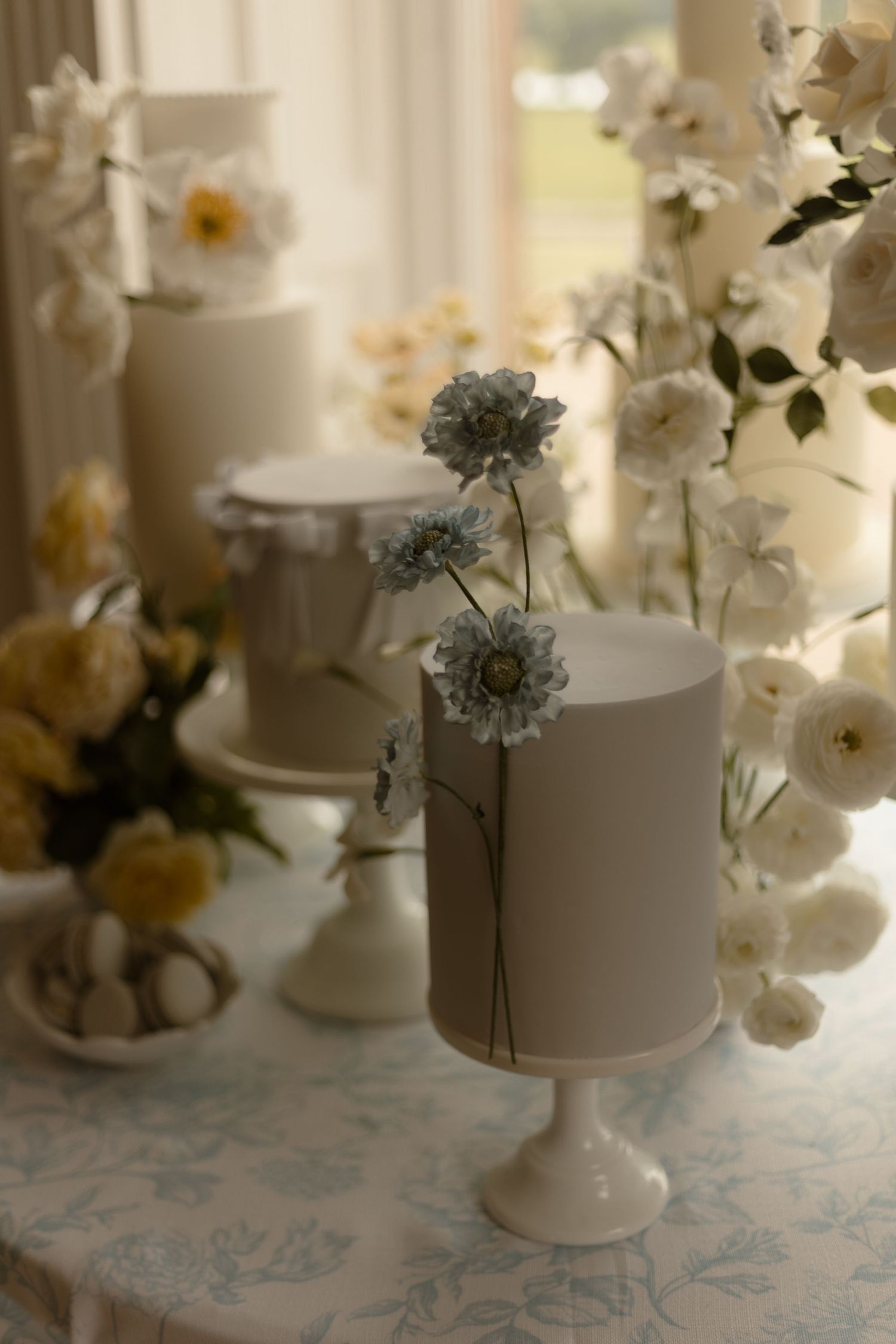 Elegant white tiered cake decorated with delicate dried flowers on a lace tablecloth in soft natural lighting.