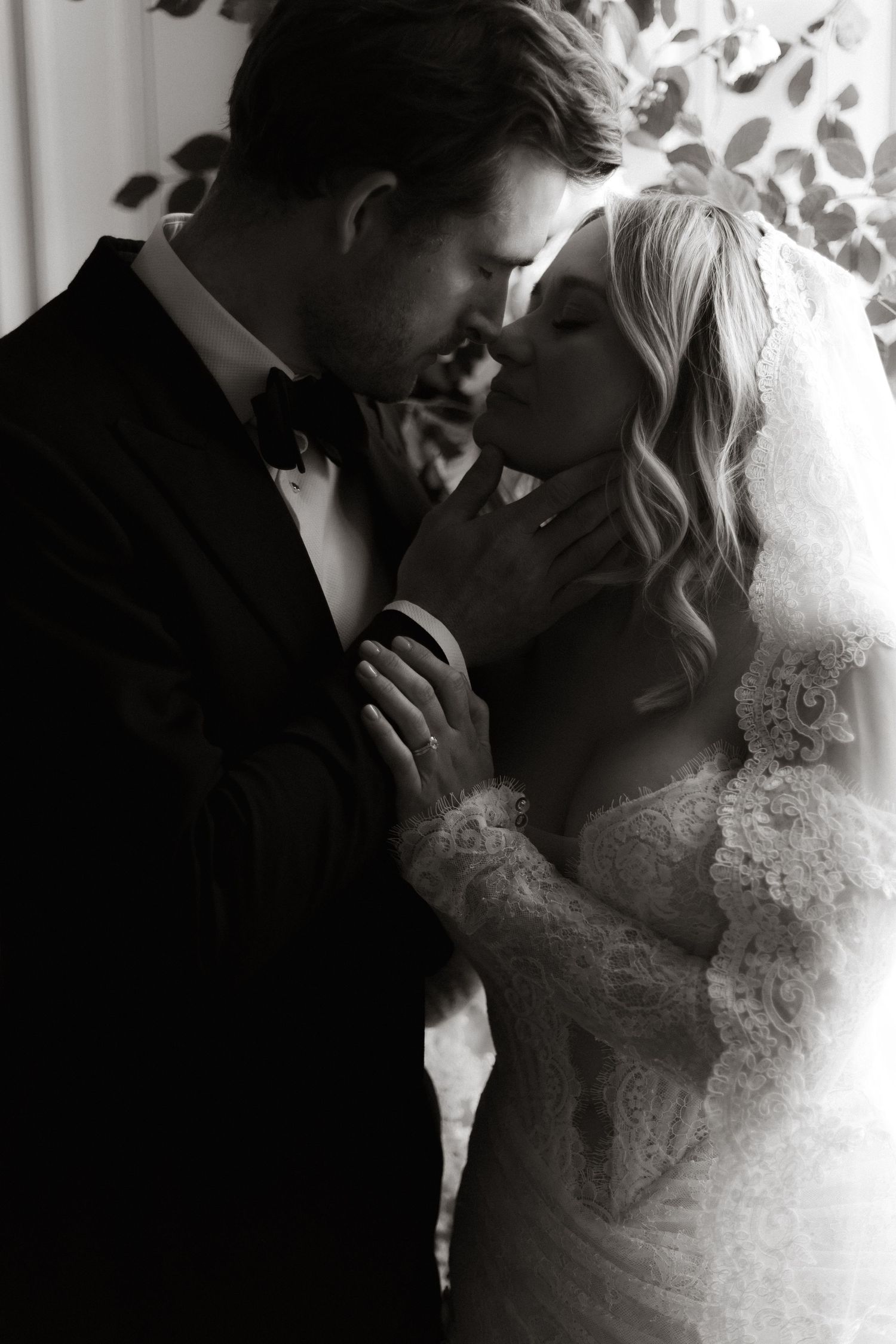Black and white intimate wedding portrait showing tender moment between newlyweds in formal attire with lace veil.