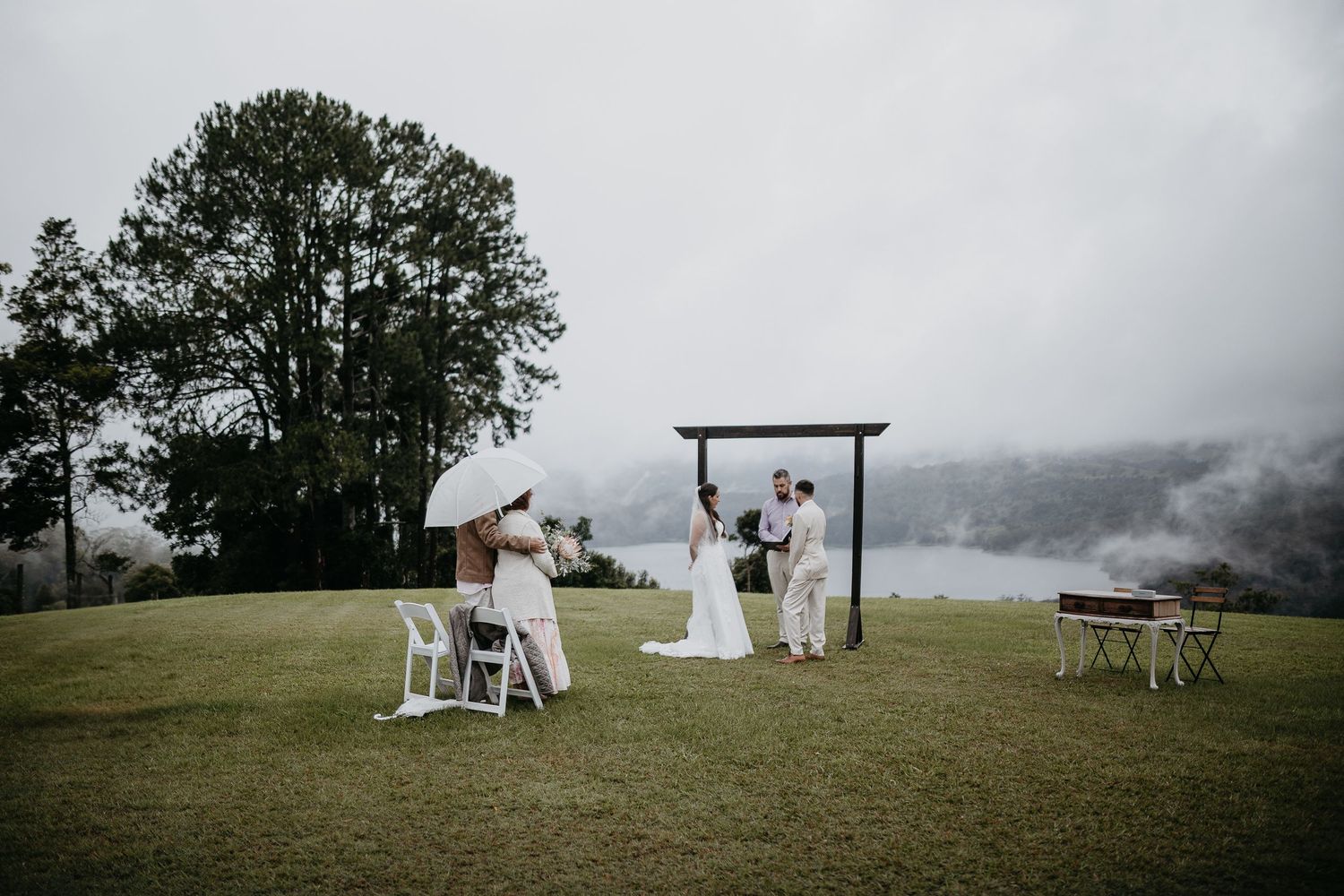 Wedding celebration on a scenic mountain hillside with misty clouds rolling across the landscape during ceremony.