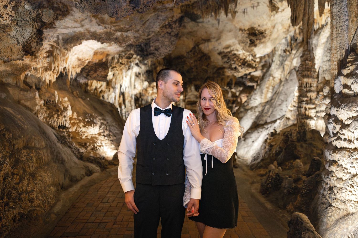 A couple dressed in formal attire share a romantic moment in a beautifully lit limestone cave.