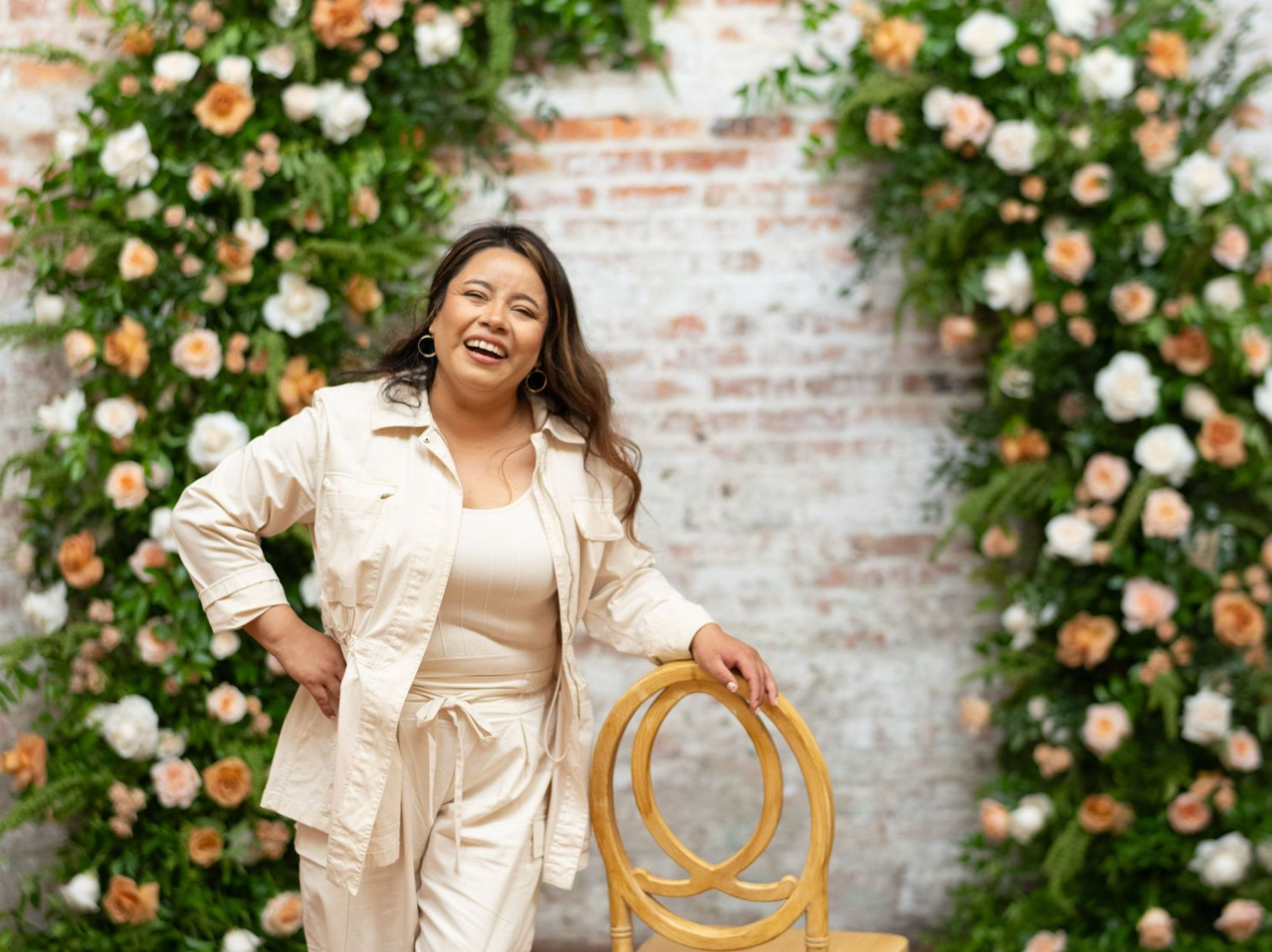 Decorative floral arch with peach and white roses against a rustic brick wall.