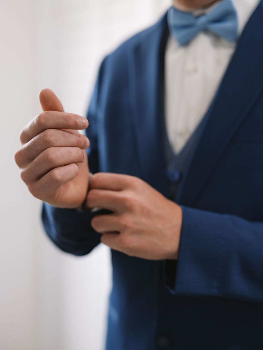 Close-up view of hands adjusting cuffs on a navy blue formal suit with matching bow tie.