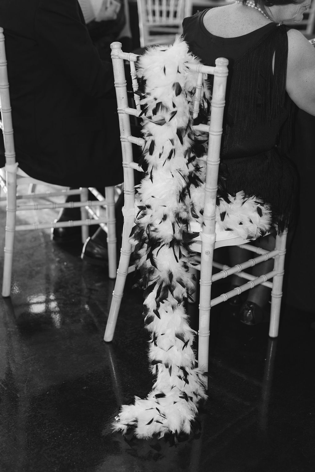 A white feather boa draped over a vintage wooden chair at what appears to be a formal event.