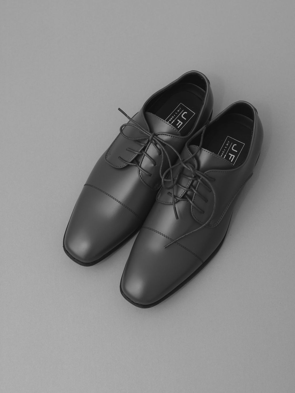 A pair of classic black leather oxford dress shoes with laces on a gray background.
