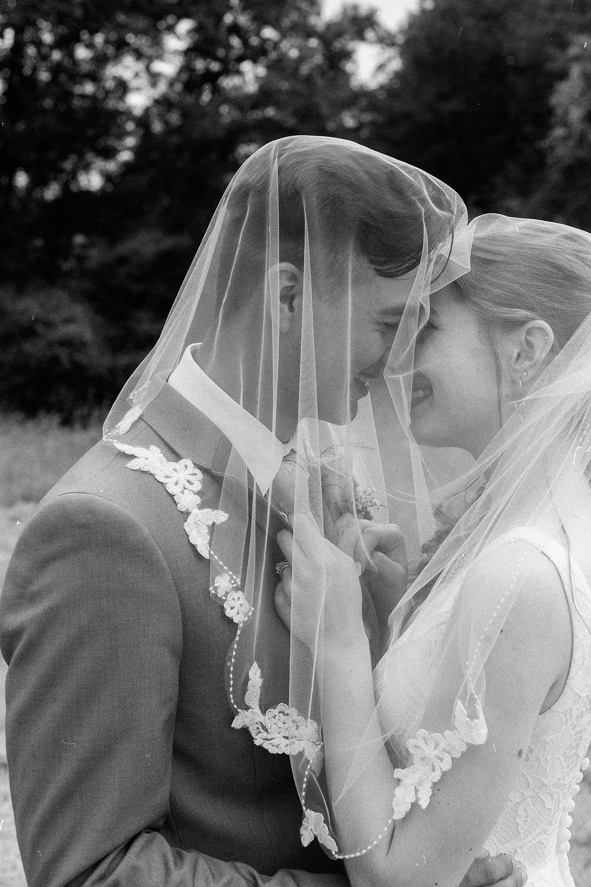 Artistic black and white portrait of newlyweds with delicate lace veil.