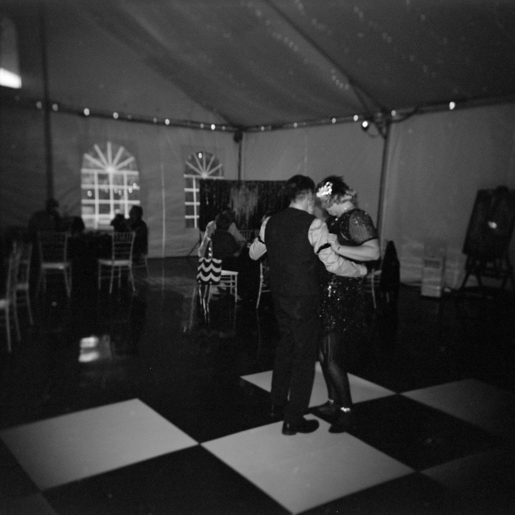 A romantic dance on a black and white checkered floor under a tent with twinkling lights in the background.