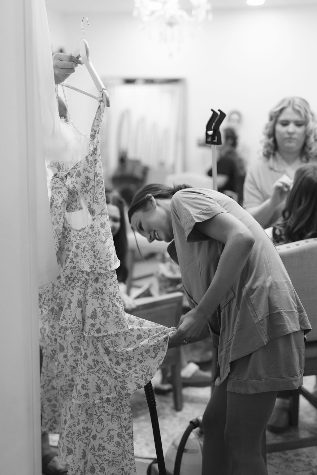 A black and white photo shows someone steaming or preparing an intricate floral patterned dress on a mannequin.