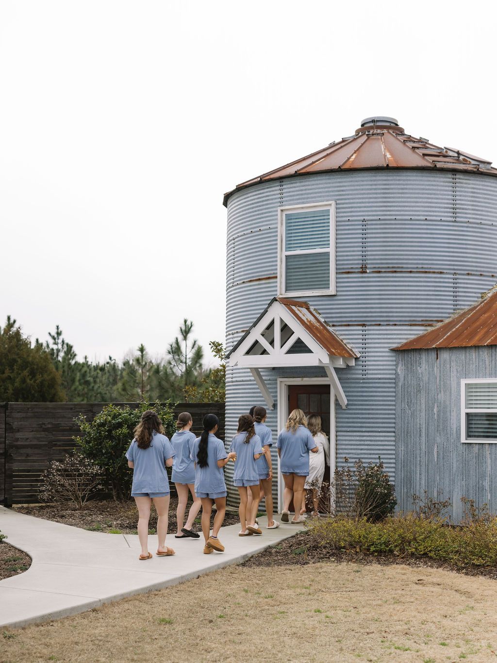 A group in matching light blue outfits walks along a pathway toward the entrance of a converted grain silo building.