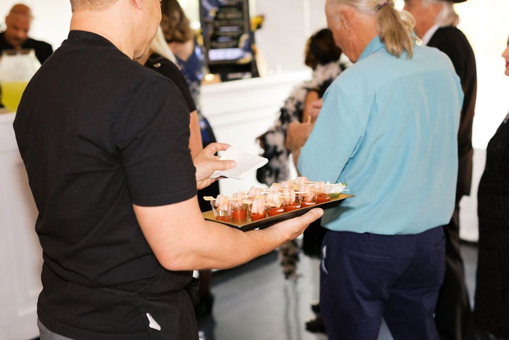 Server carrying tray of appetizers at an indoor event with guests in background.