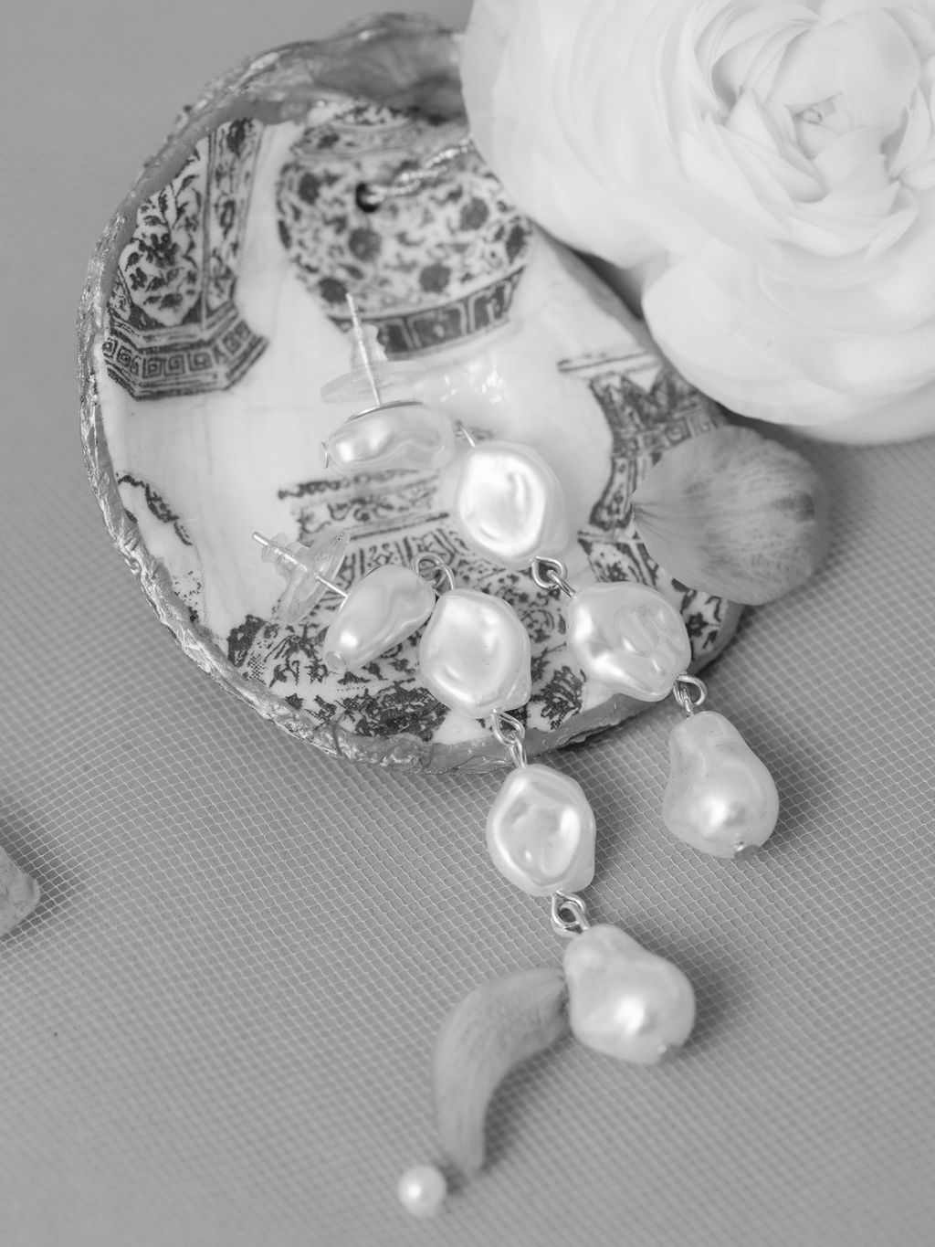 Elegant silver brooch with dangling pearl accents and delicate filigree detail against soft grey fabric and white rose.