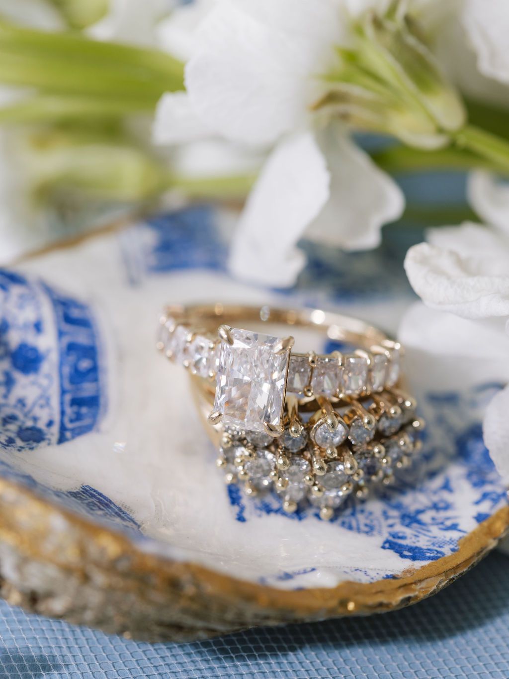 Beautiful diamond wedding rings stacked on vintage blue and white china with white lilies in the background.