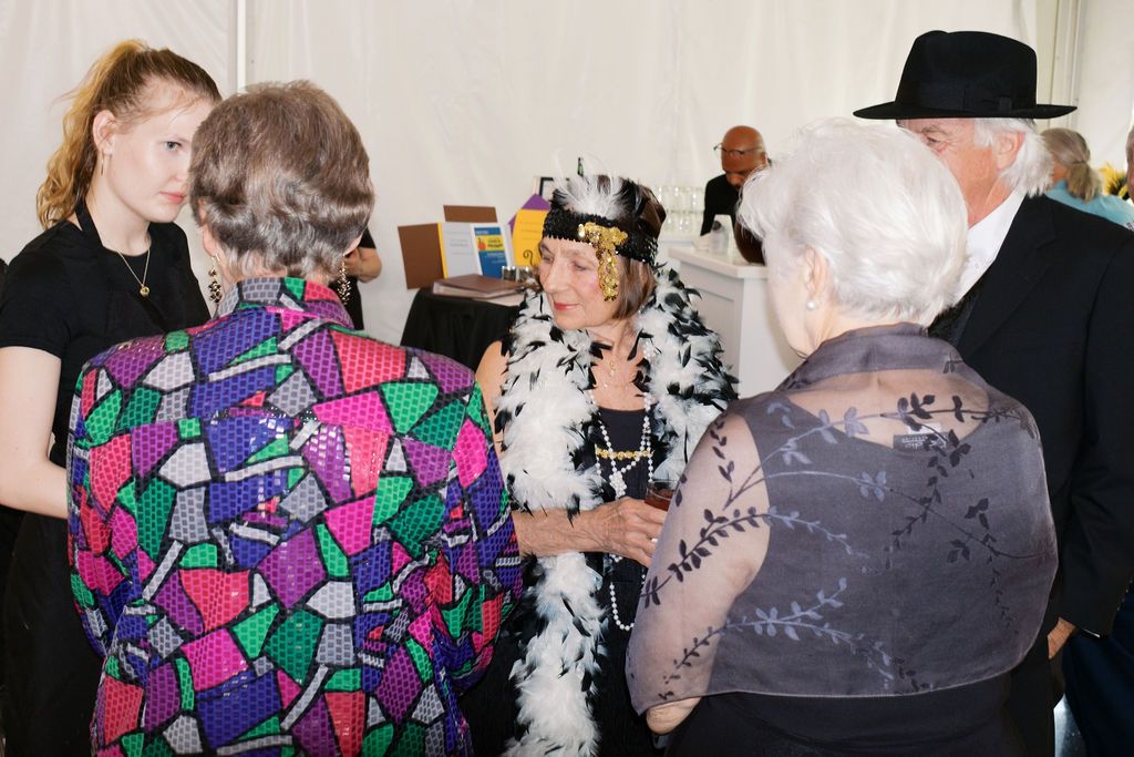 People gathered at an indoor event with some wearing colorful patterns and feather boas in a casual social setting.
