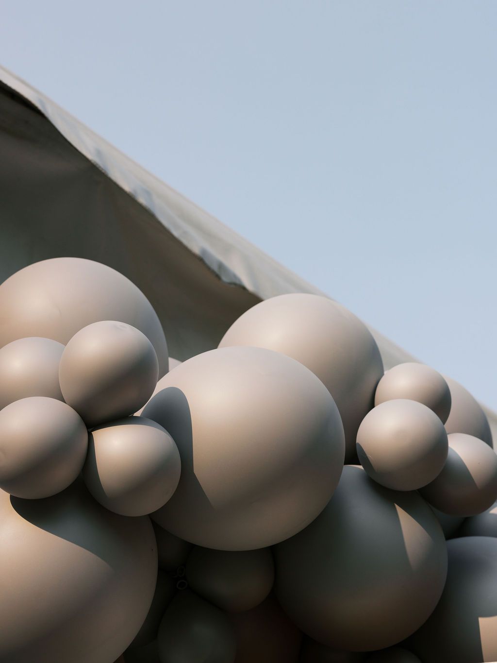 Abstract architectural detail featuring spherical shapes in light beige tones mounted on a curved surface against blue sky.