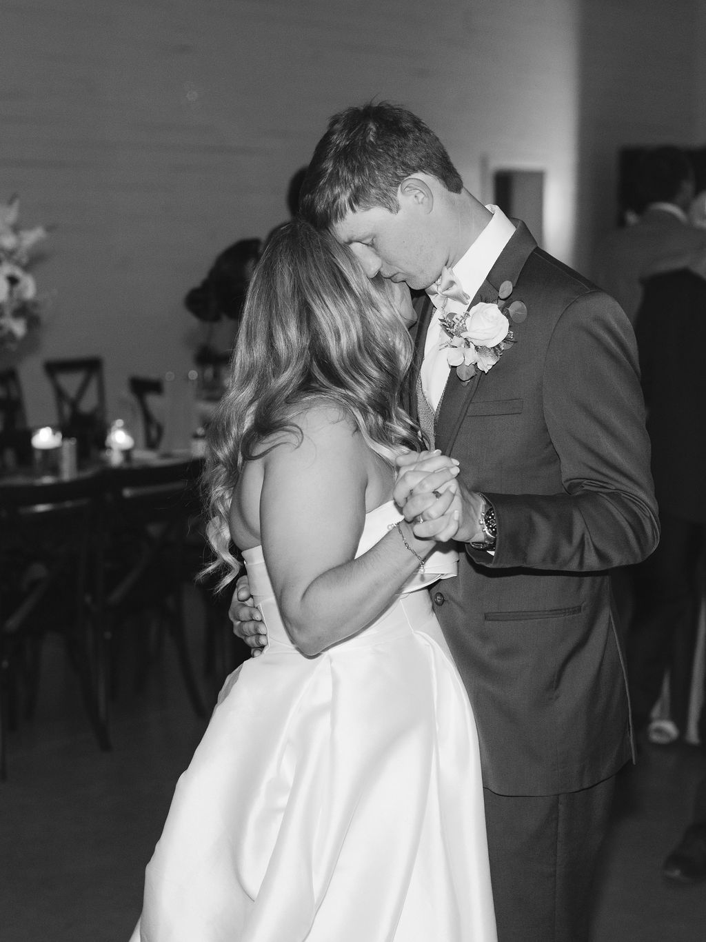A couple shares an intimate first dance at their wedding reception, captured in black and white photography.
