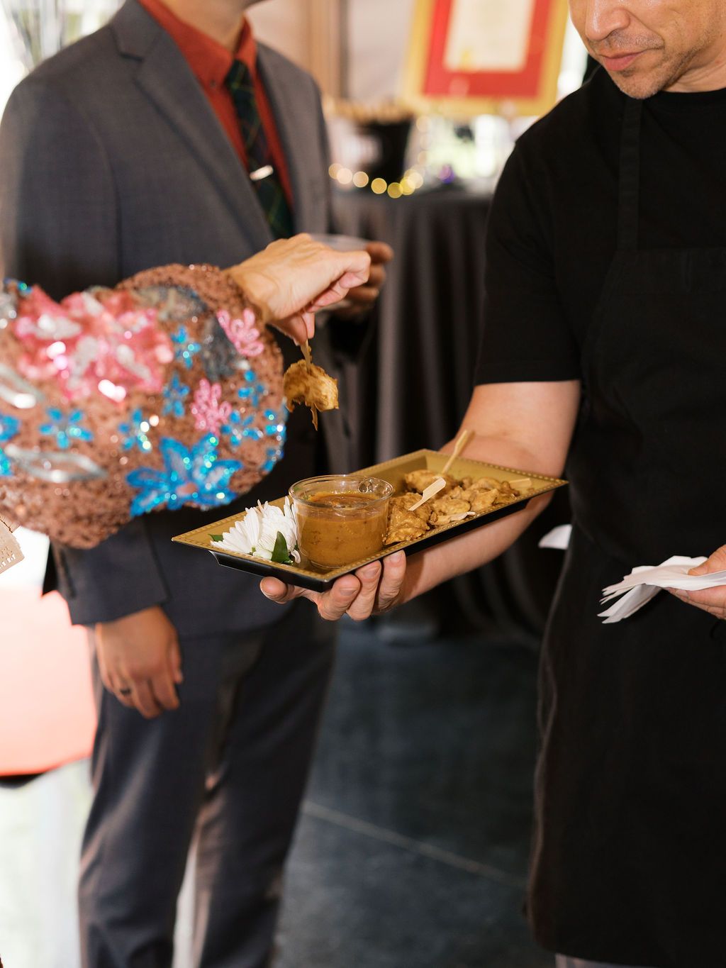 Server holding wooden tray with appetizers and dipping sauces at an upscale catered event.