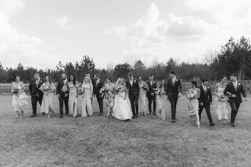 A black and white image of a wedding party walking together in a line formation across a grassy field.