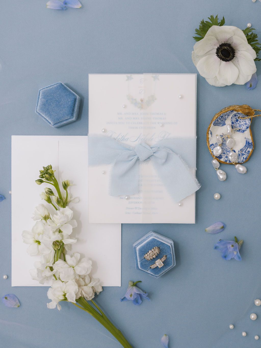 Wedding invitation suite in white and light blue with floral accents and hexagonal details arranged on pale blue surface.