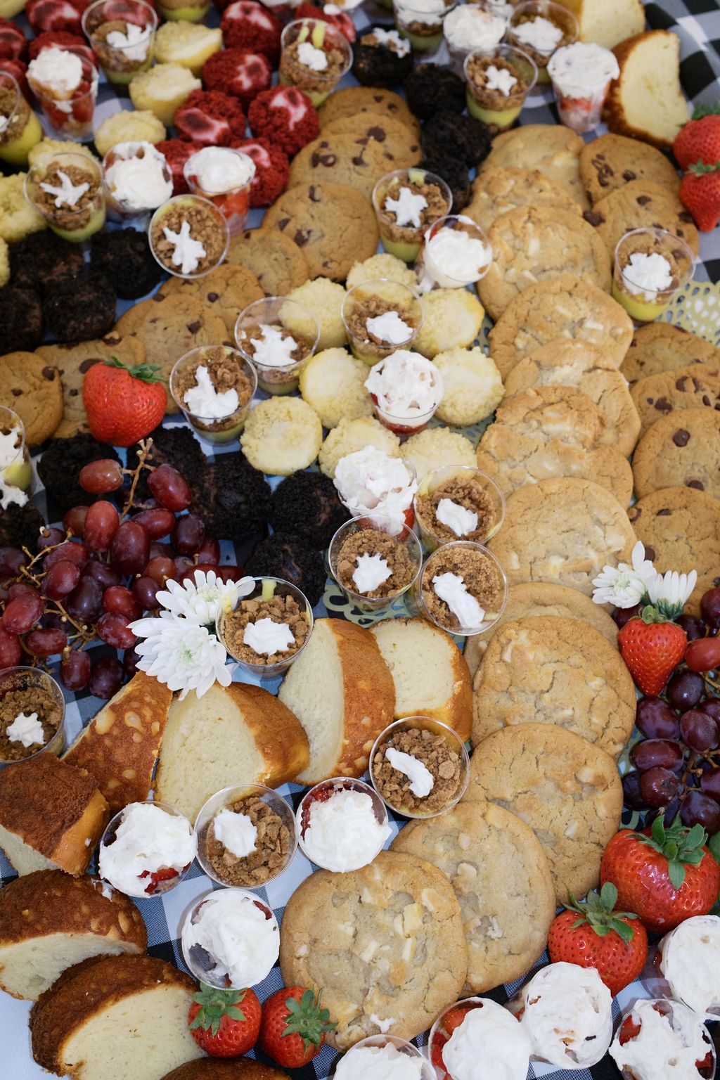 A dessert platter featuring chocolate chip cookies, red grapes, strawberries, and cream-filled pastry cups.