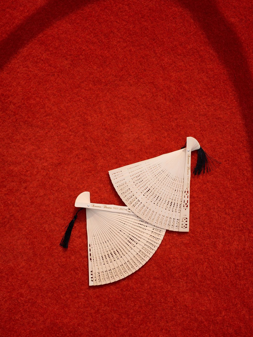 Two delicate white folding hand fans with black handles arranged artistically on a vibrant red background.