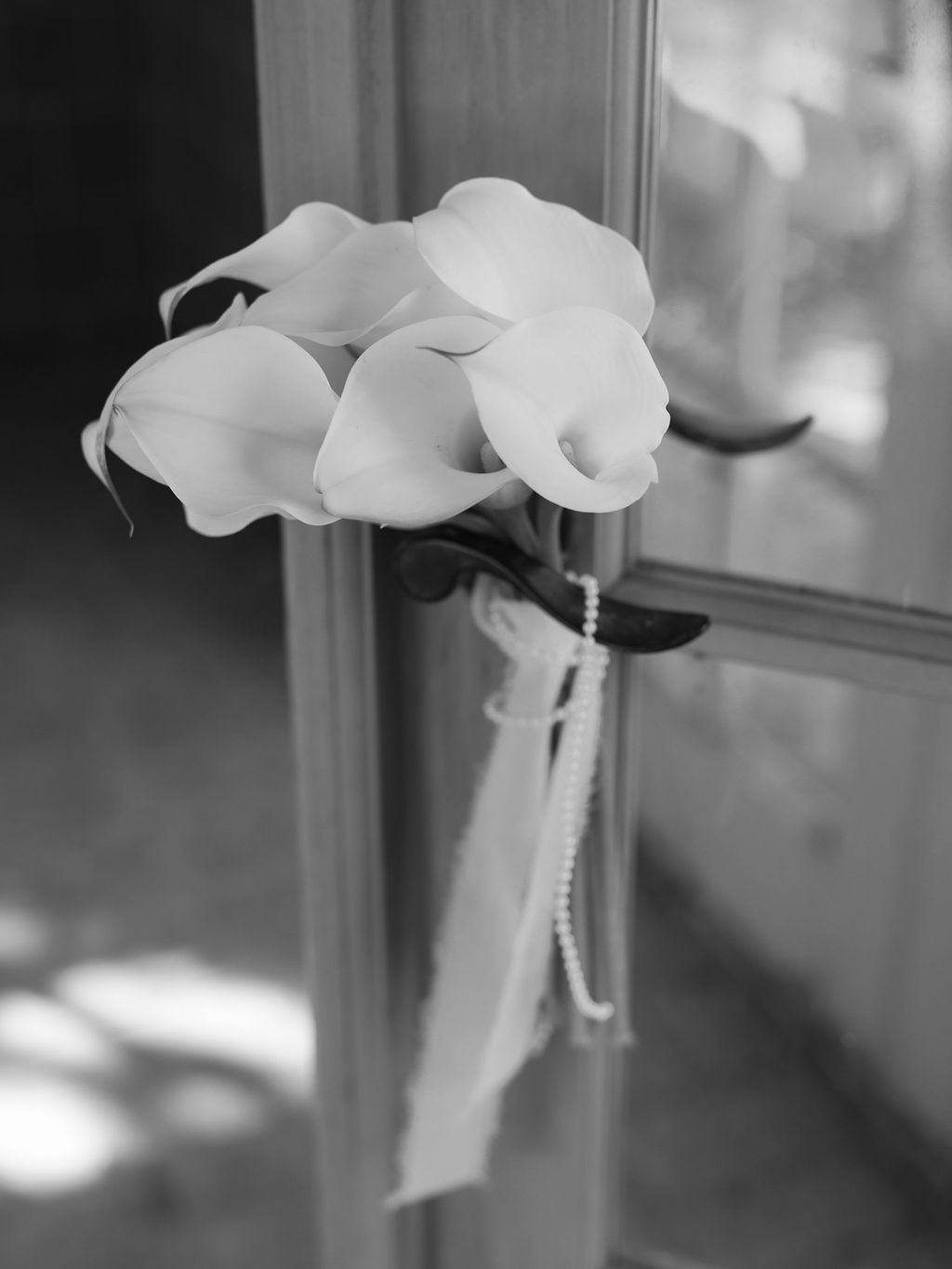 Black and white photograph of calla lilies in a window with soft natural light.