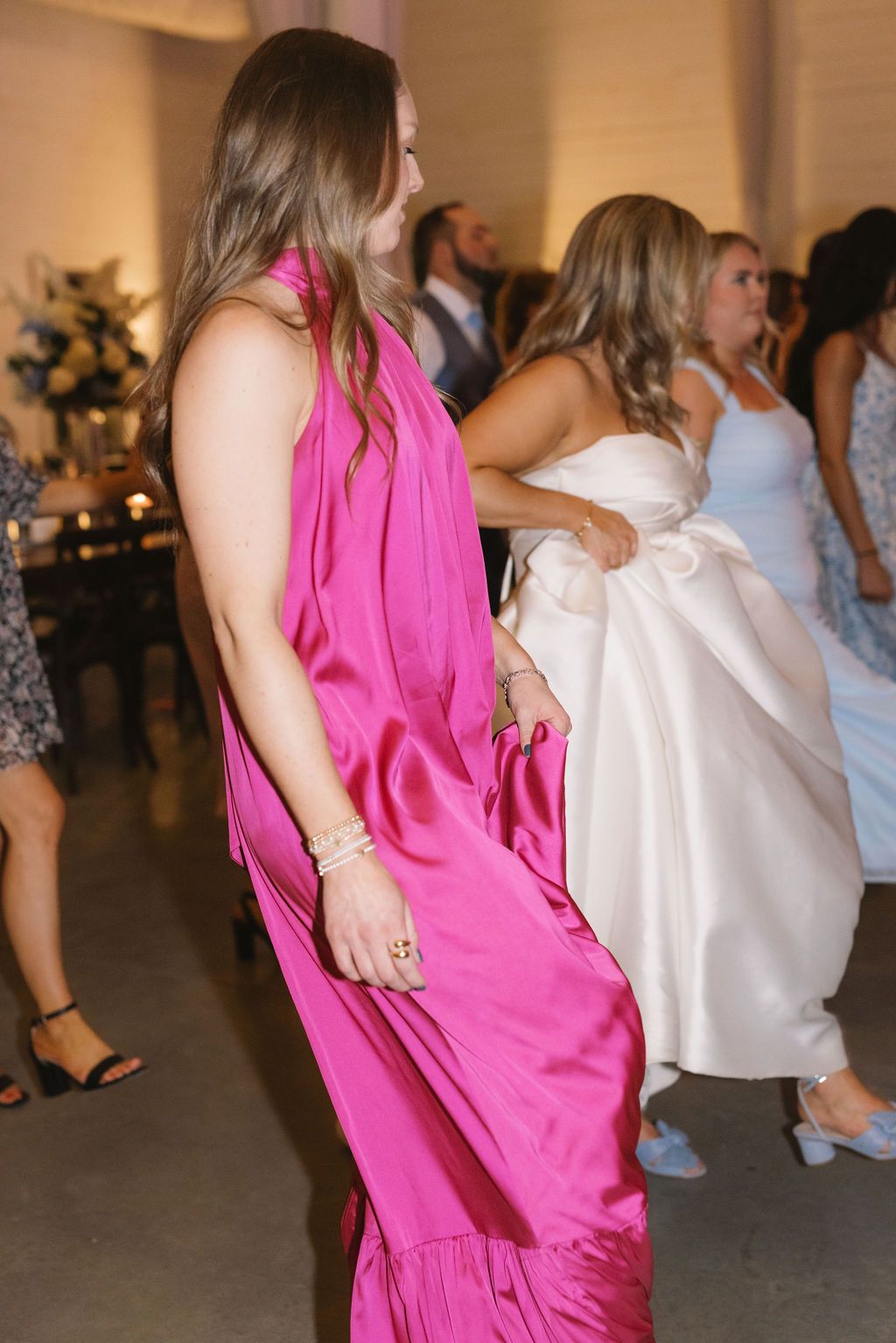 People dancing at a celebration event with someone wearing a bright pink flowing dress in the foreground.