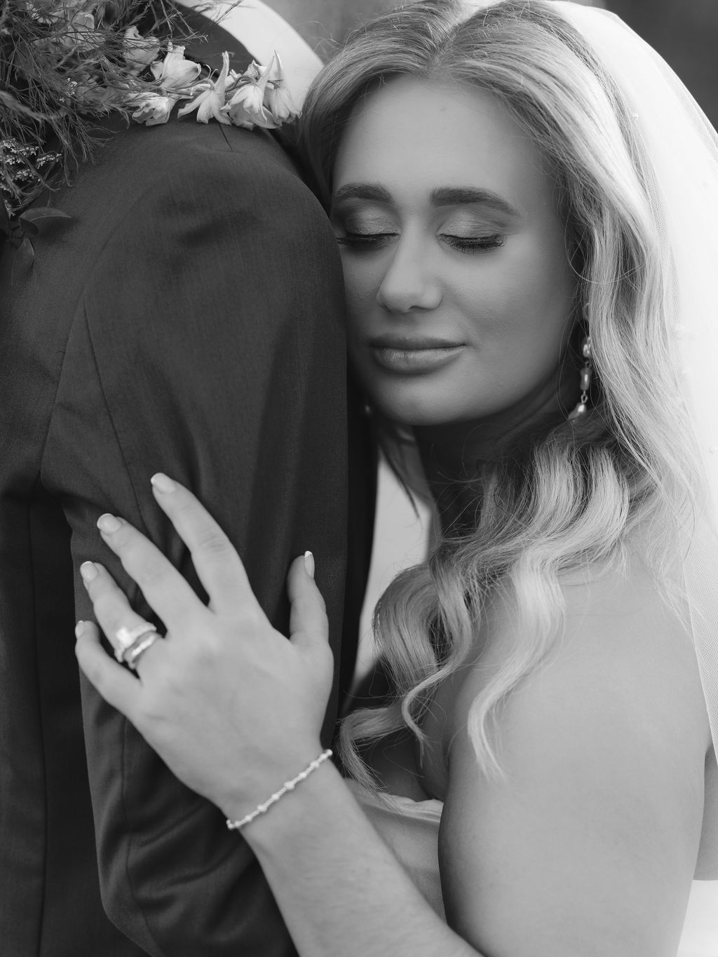 A tender black and white portrait of a bride in an elegant dress with long blonde hair and sparkling jewelry.