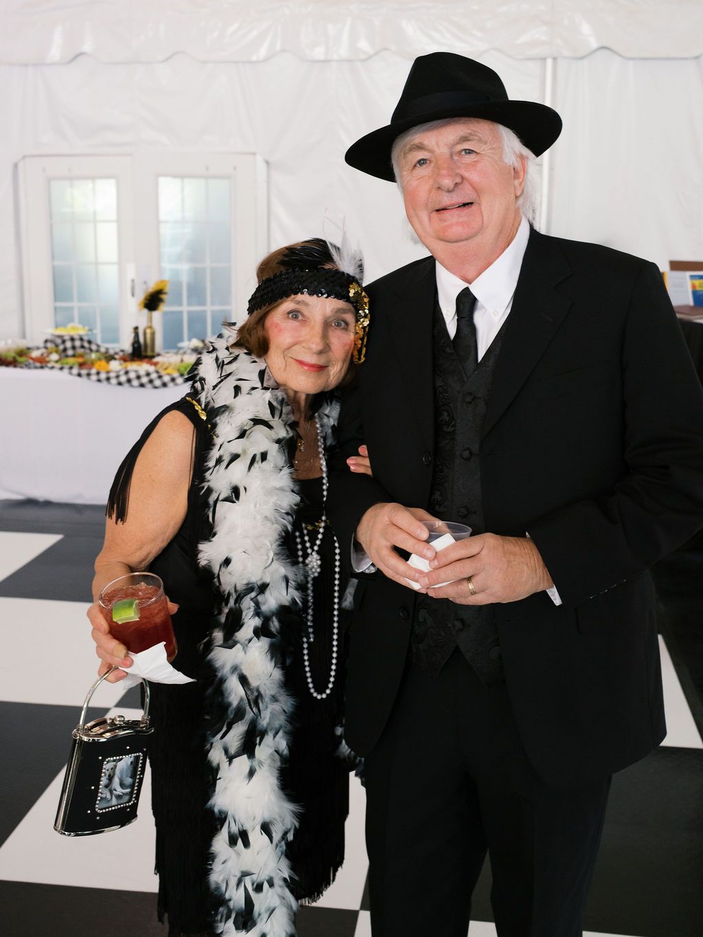 A couple dressed in 1920s style attire with flapper feather boa and formal black suit at a party celebration.