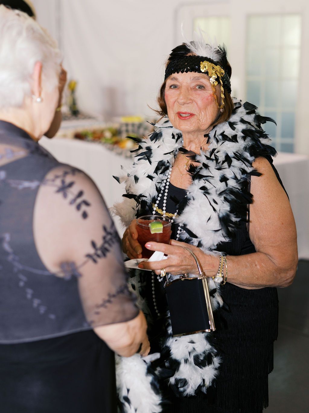 Reveler at a party wearing a flapper-style headpiece, black and white feather boa, and holding a drink.
