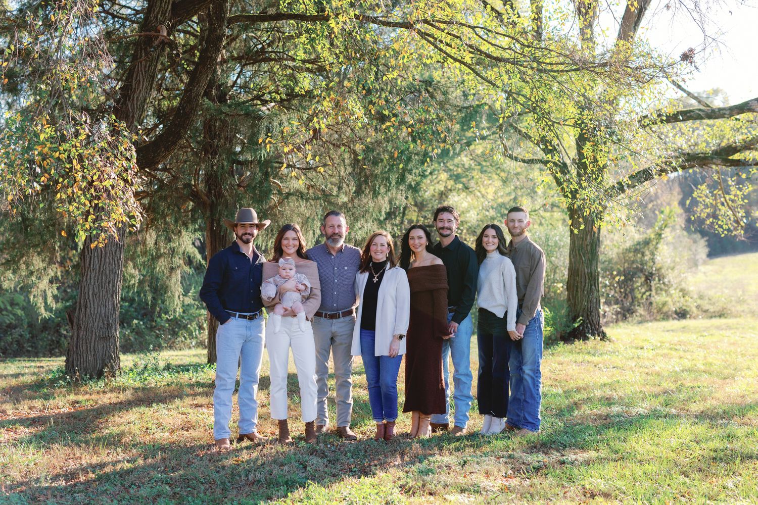 Group portrait of people standing together outdoors under autumn trees in a scenic setting.