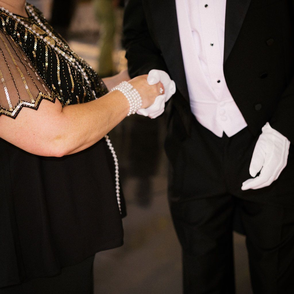 Cropped formal attire view showing black tie evening wear with white gloves and elegant beaded details.