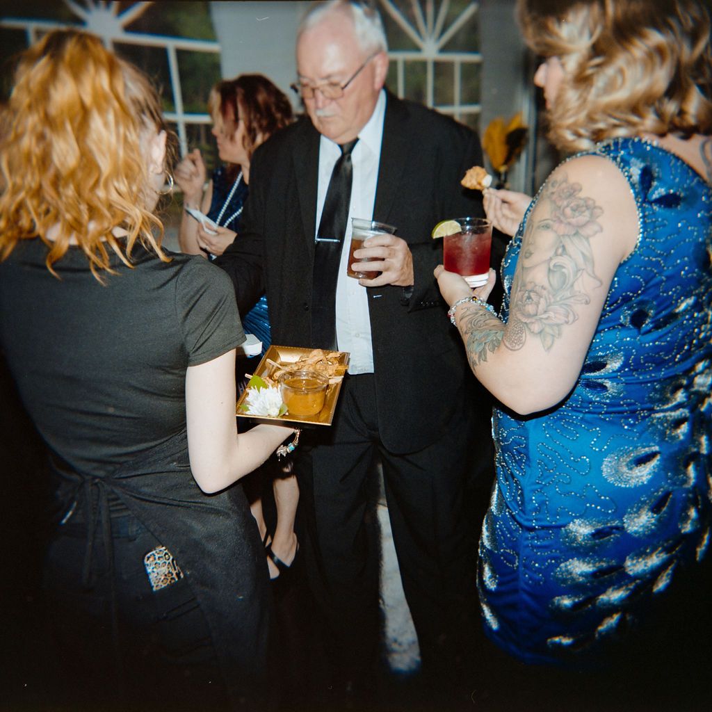 People mingling at an evening social gathering with drinks and food while wearing formal attire.