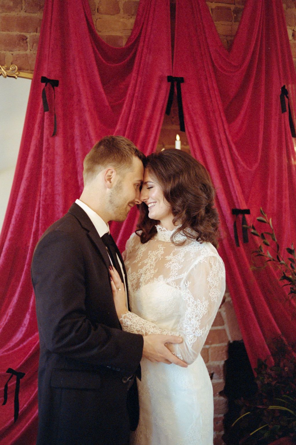 Intimate wedding portrait against brick wall with flowing red curtains.