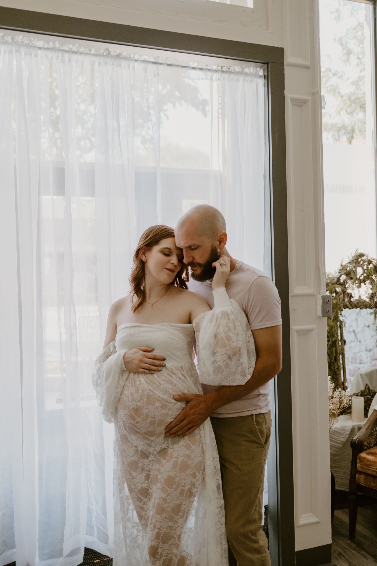 An intimate maternity photo of a couple by a window in soft natural light.
