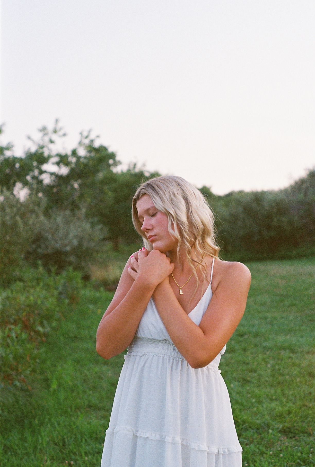 Woman in white sundress poses thoughtfully in outdoor setting at dusk.