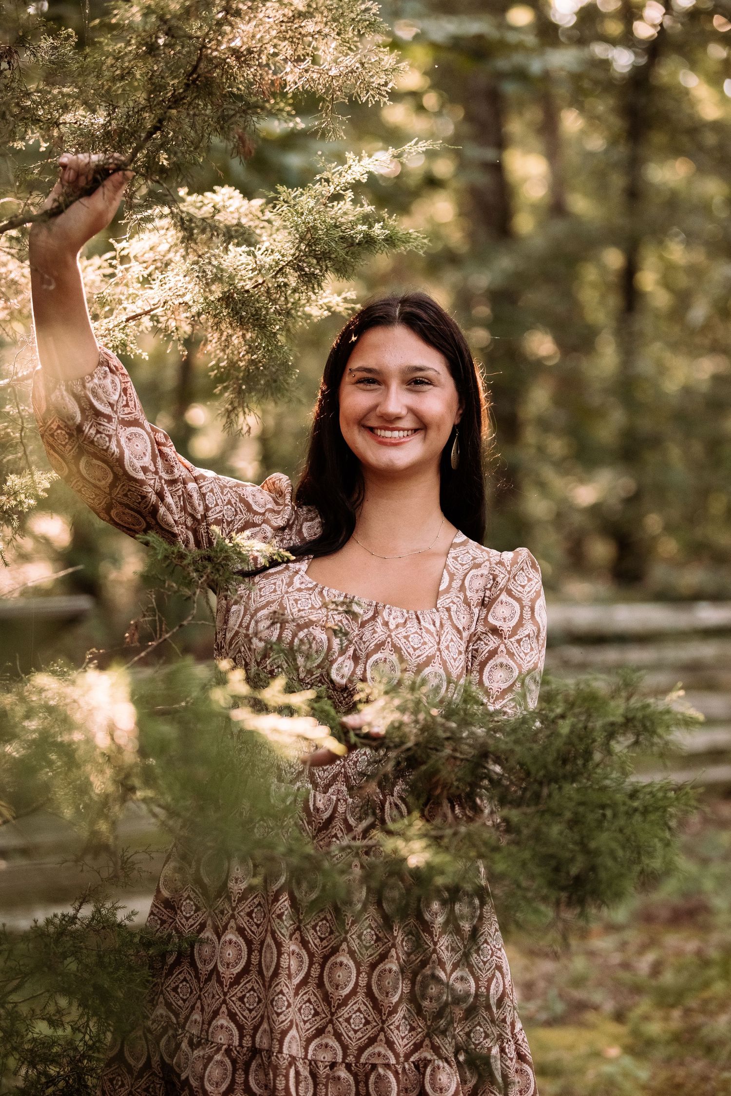 A woman in a floral dress poses joyfully in a sunlit forest setting, creating a series of candid outdoor portraits.