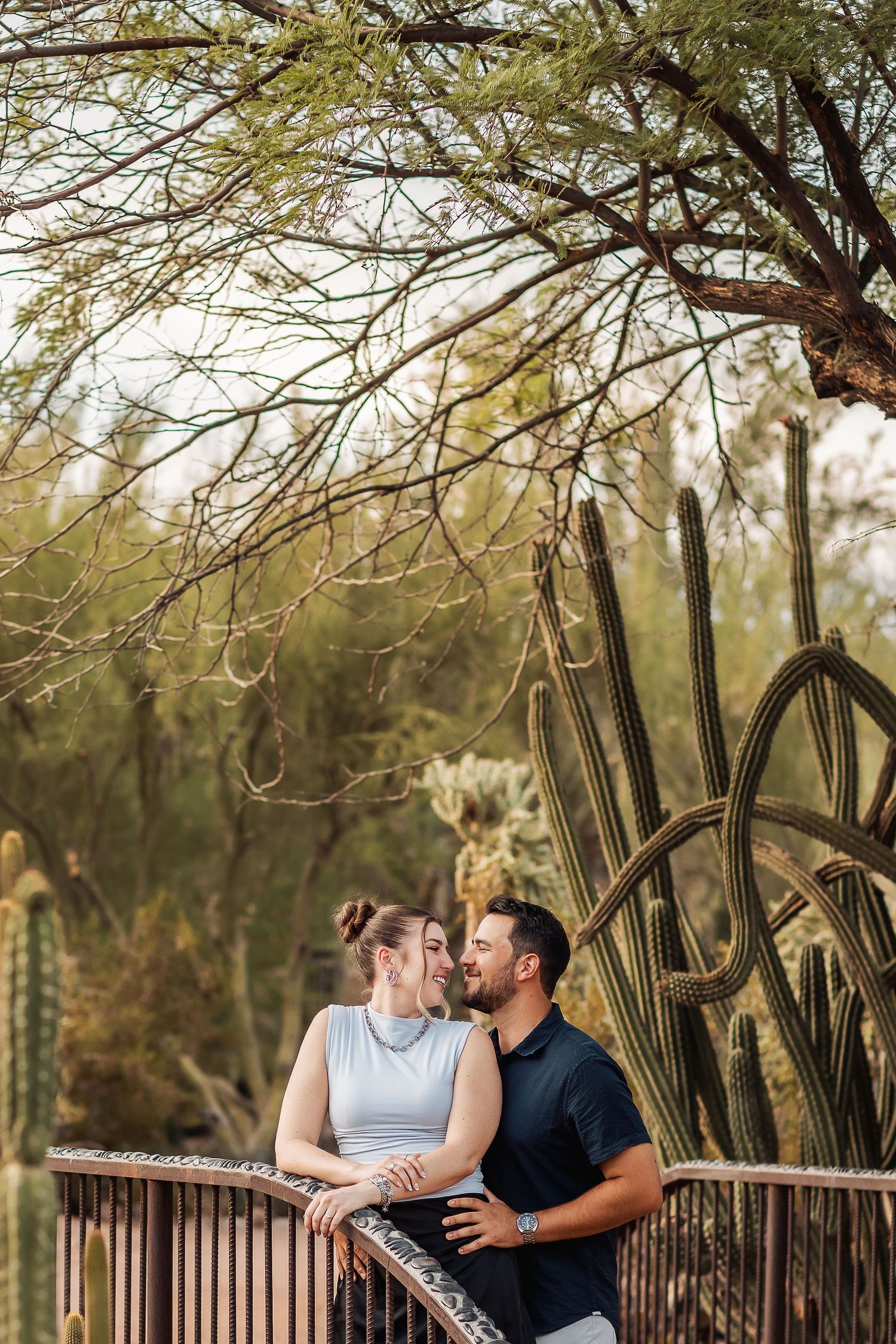 A couple shares tender moments while standing together near tall saguaro cacti in a desert landscape setting.