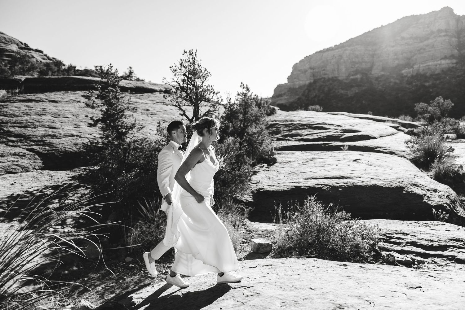A couple in flowing white outfits dance together on red sandstone cliffs against a desert backdrop.