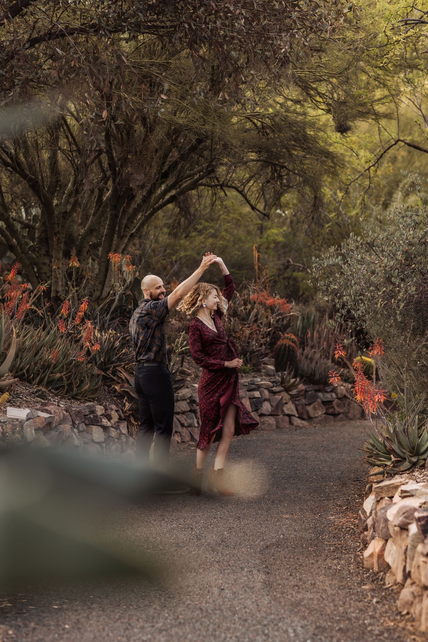 A couple dances together on a garden path surrounded by autumn foliage and decorative rock walls.