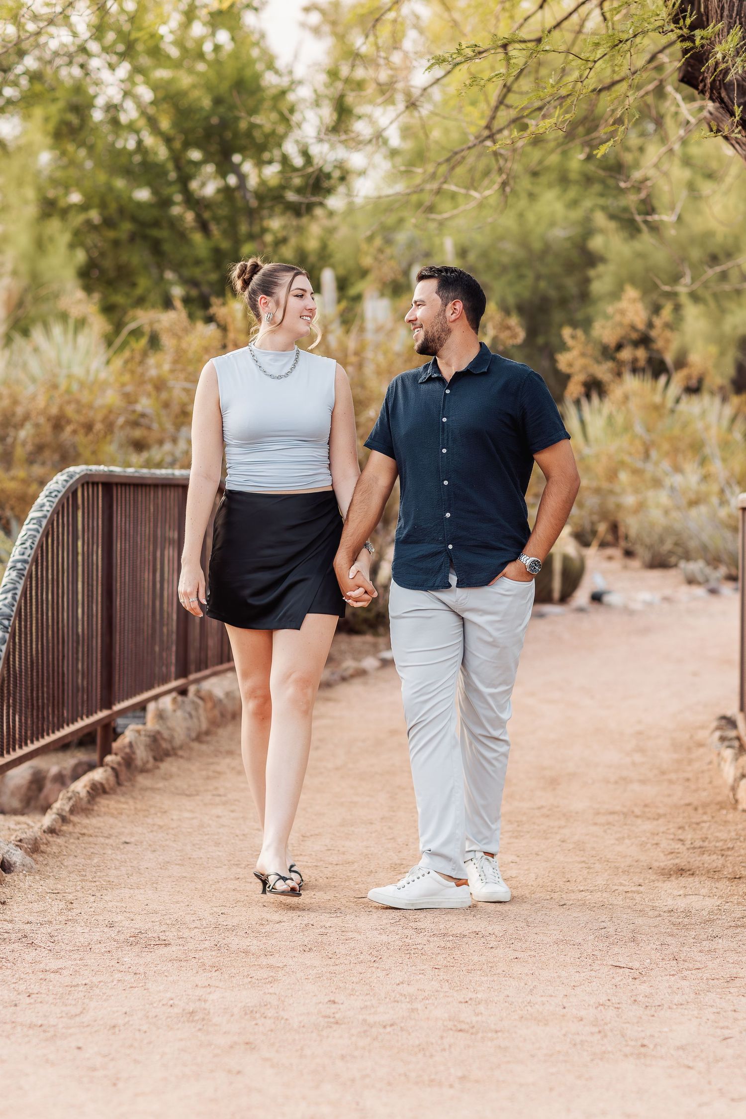 A couple walks hand in hand along a desert trail during a warm sunset photoshoot in the American Southwest.