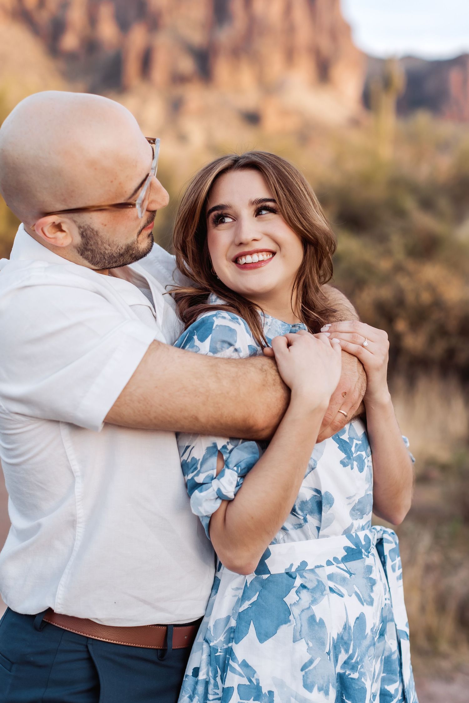 A loving couple embraces in front of desert mountains during sunset.