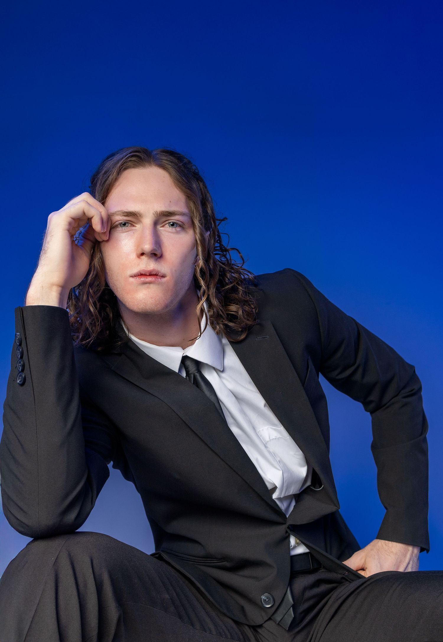 Low angle view against blue sky of figure in black suit and white shirt adjusting their outfit in three poses.