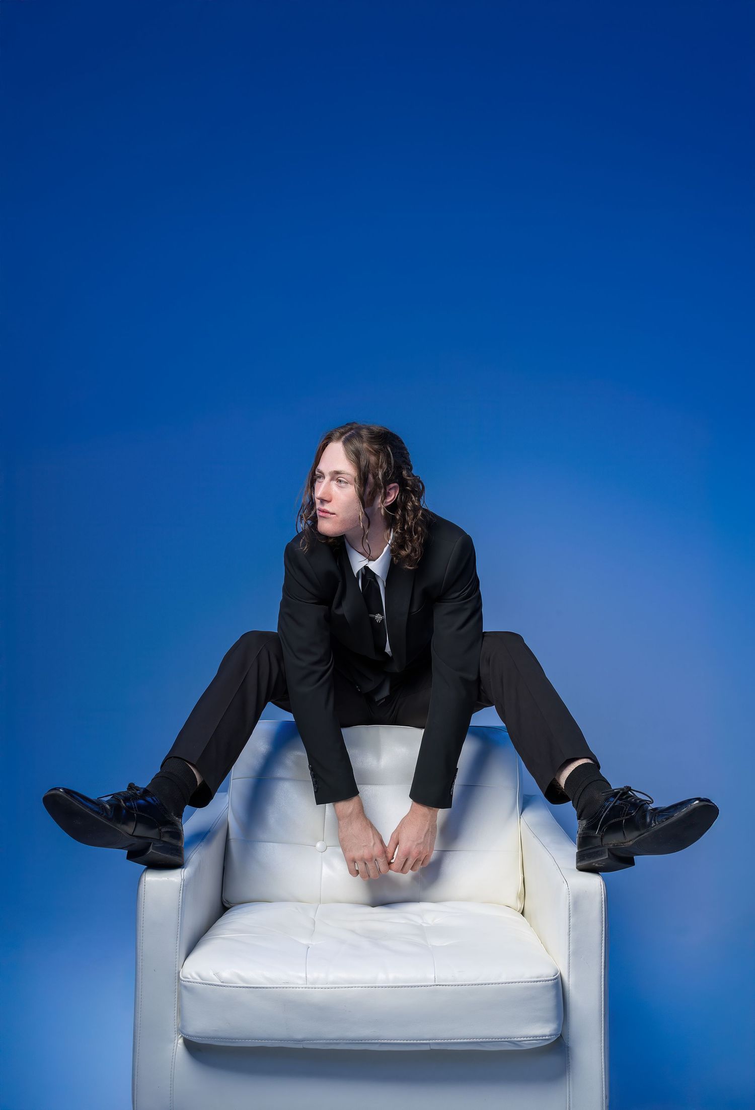 Person in dark suit reclining awkwardly on a white cushioned surface against blue background in artistic poses.