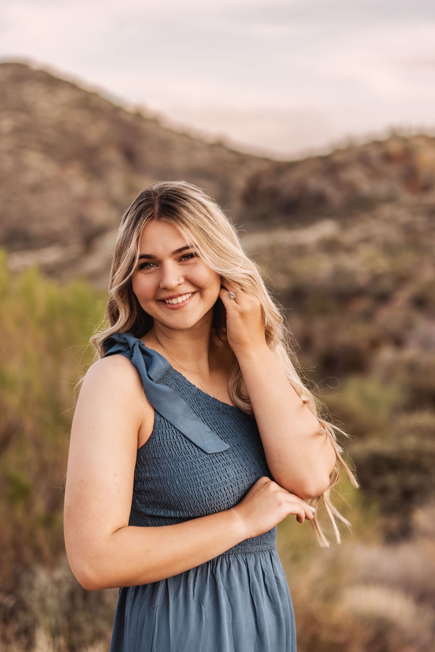 Smiling woman in blue dress poses against desert mountain landscape during golden hour portrait session.