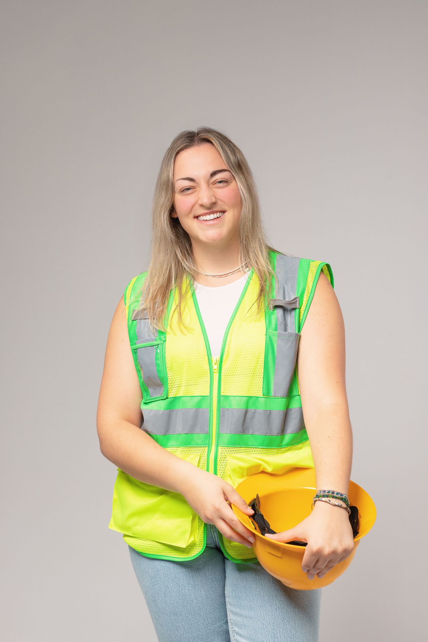 Construction worker wearing high visibility safety vest smiling while holding yellow hard hat in sequence of poses.