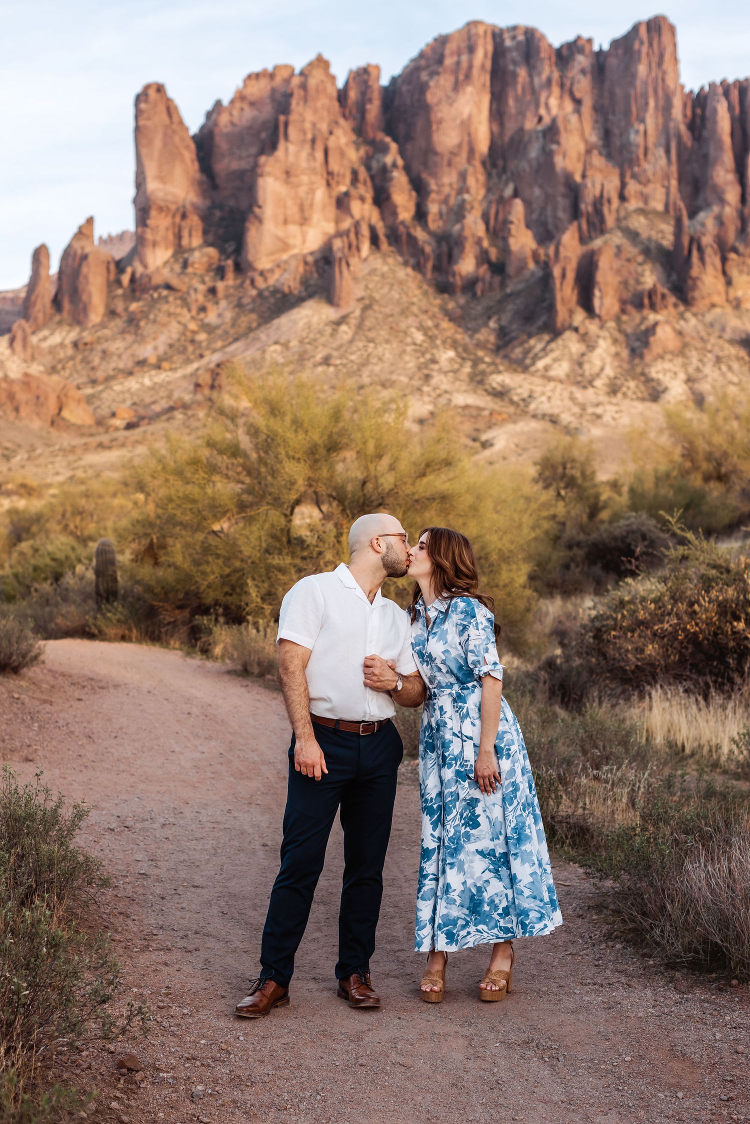 Couple sharing romantic moment on dirt path with stunning Superstition Mountains backdrop in Arizona.