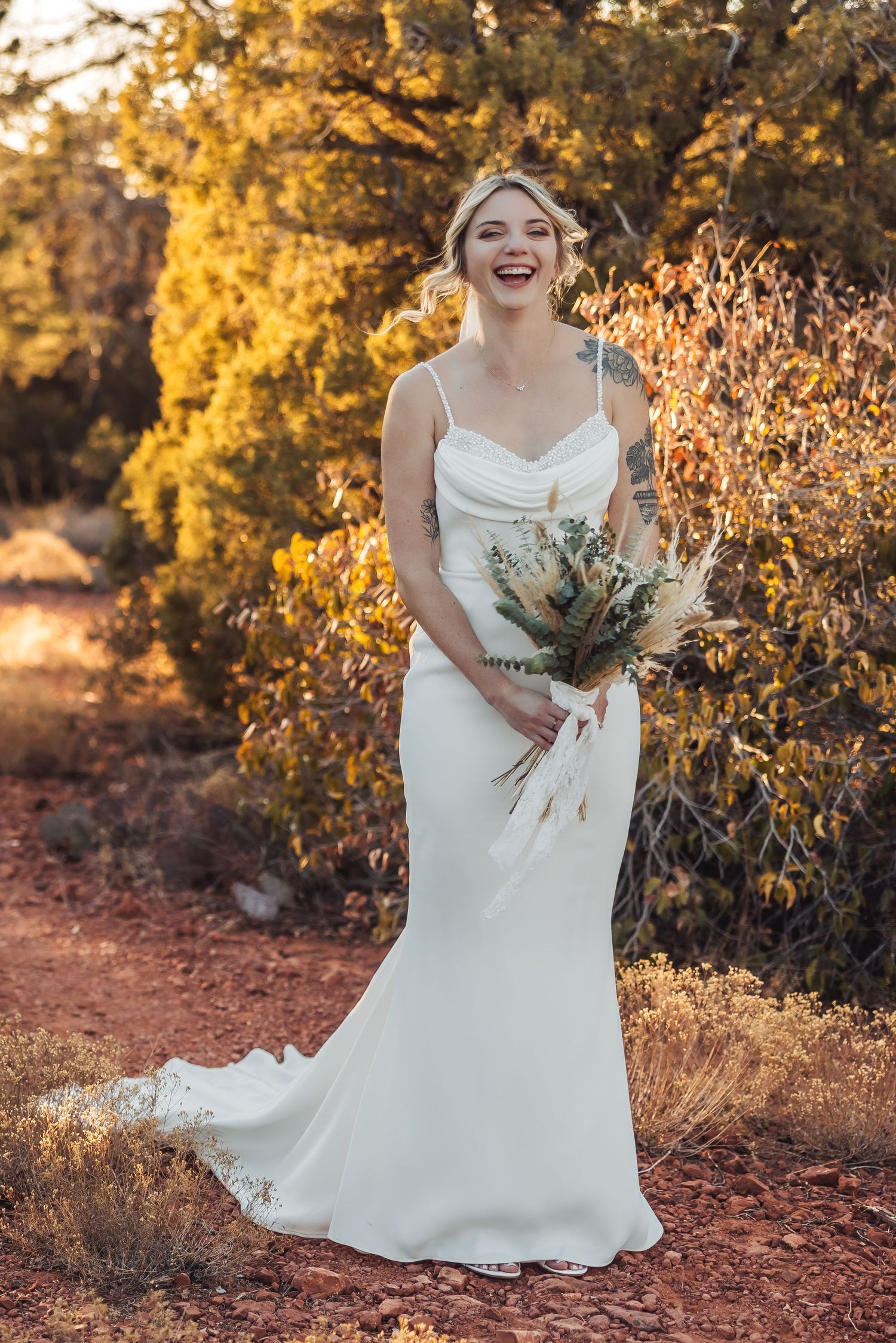 Joyful wedding portrait amidst desert foliage with warm autumn sunlight filtering through.