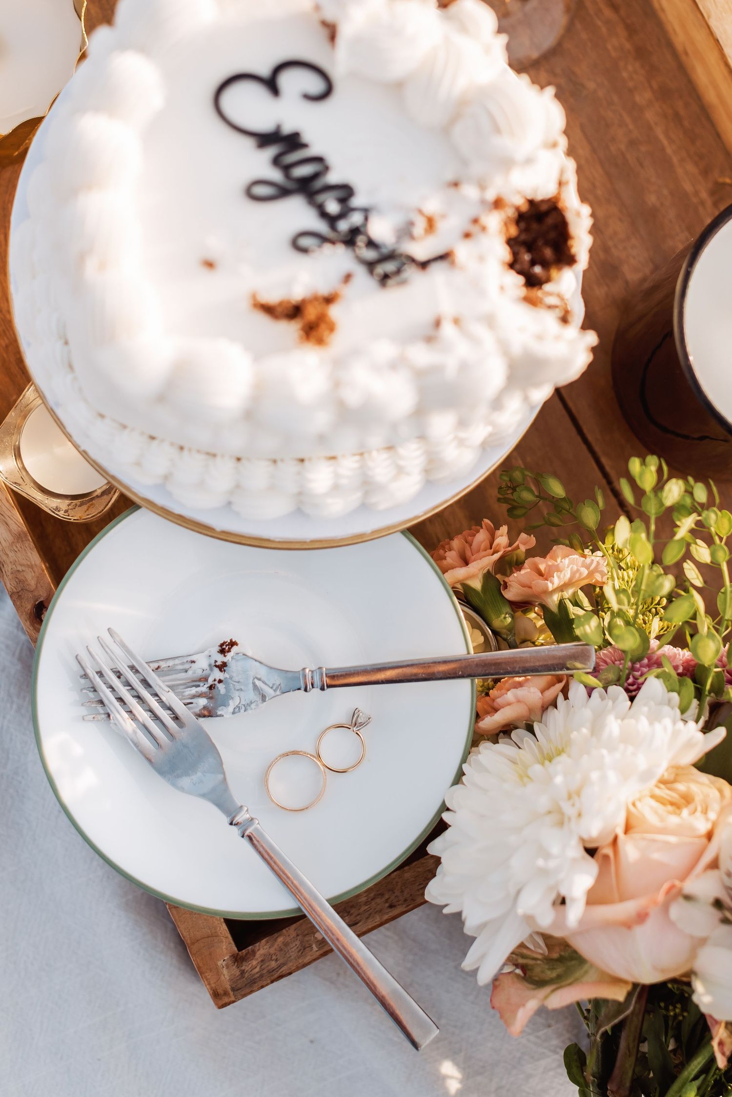 Wedding cake, rings, and floral decor artistically arranged on rustic wooden serving tray.