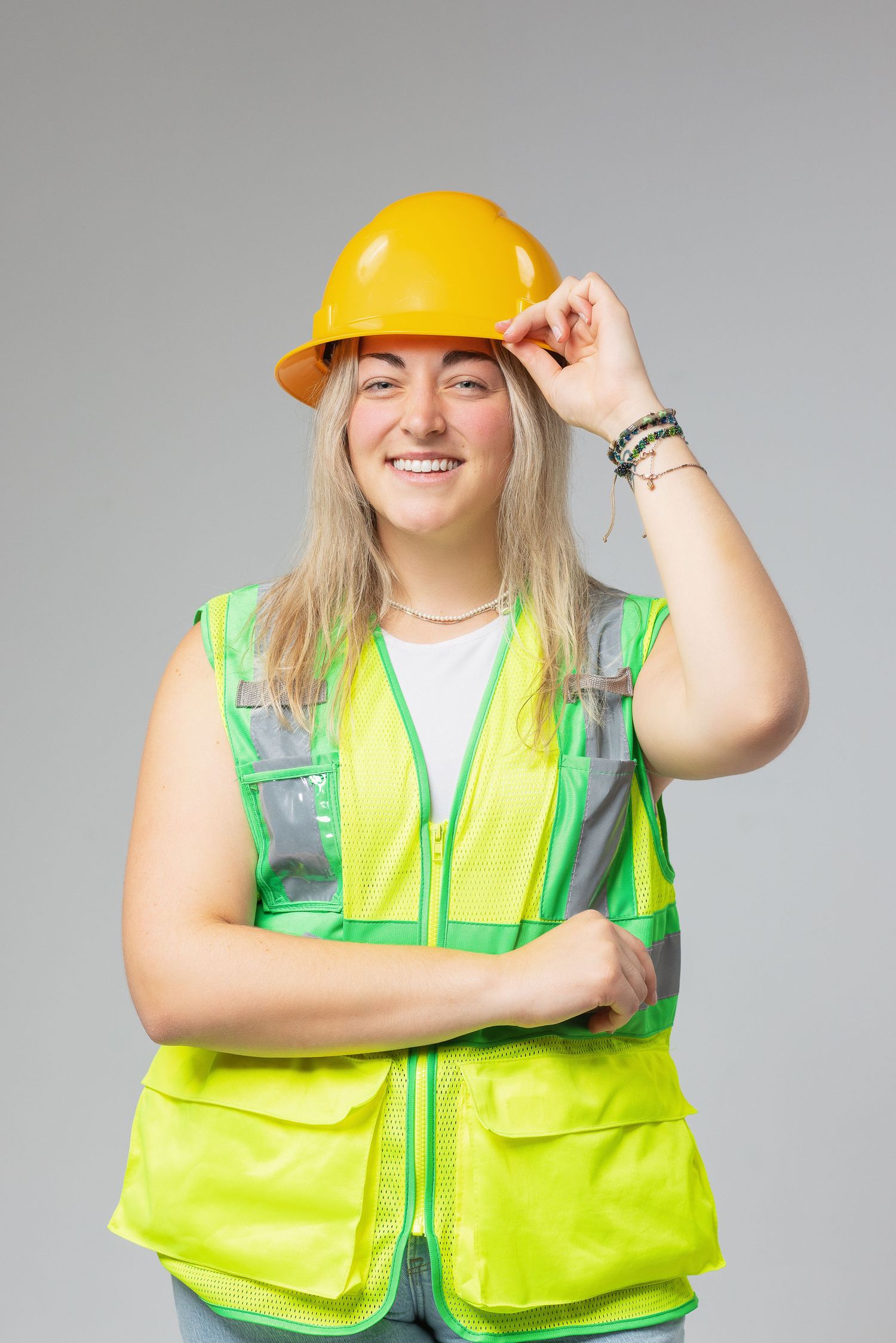 Construction worker wearing bright yellow hardhat and reflective safety vest smiles while adjusting helmet.