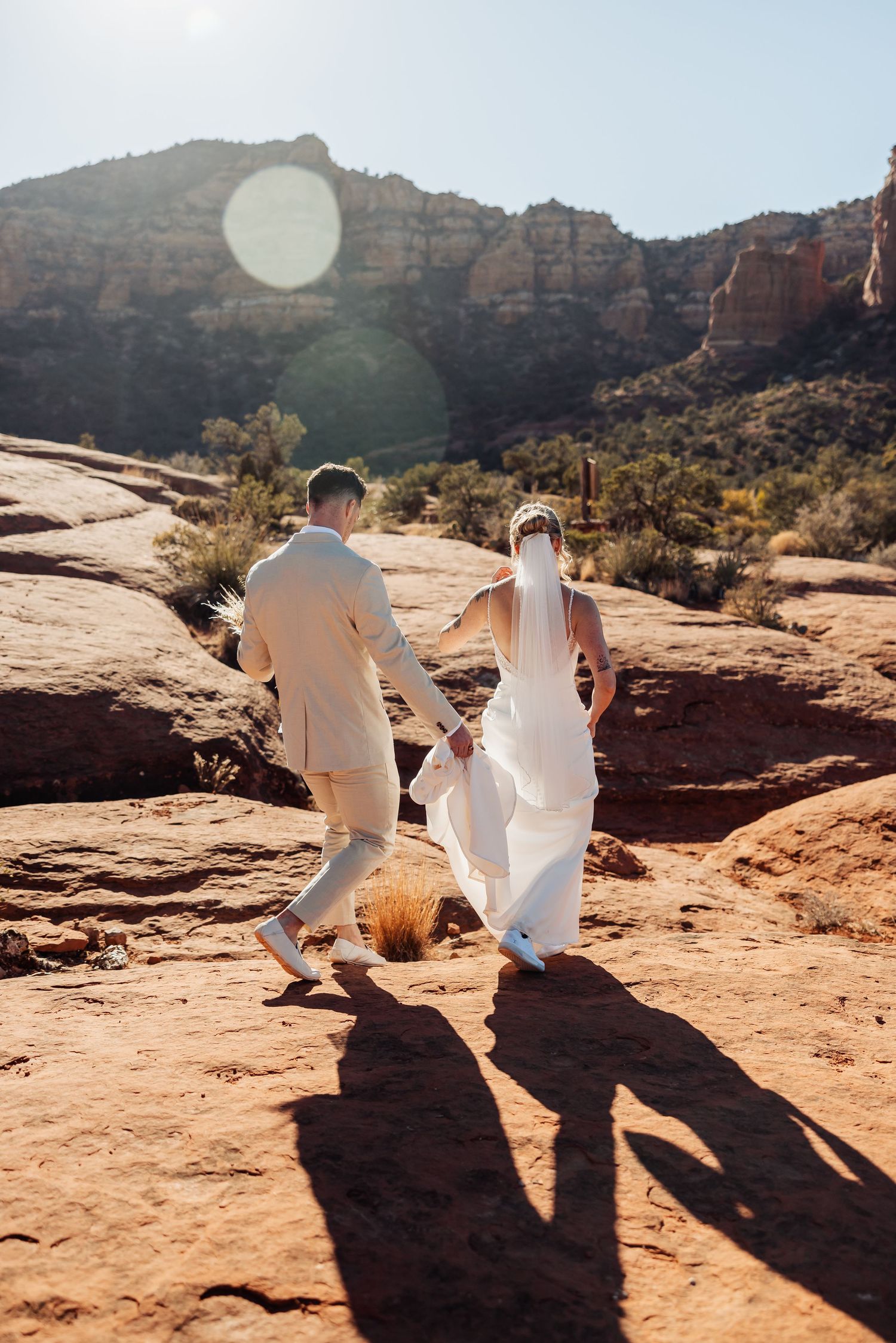 Two people sit together on red sandstone rocks overlooking scenic desert canyon views on a sunny afternoon.